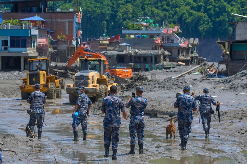 Des policiers népalais observent des engins de terrassement déblayer les débris d'une crue soudaine dans le district de Nuwakot, au Népal, le jeudi 27 août 2026.