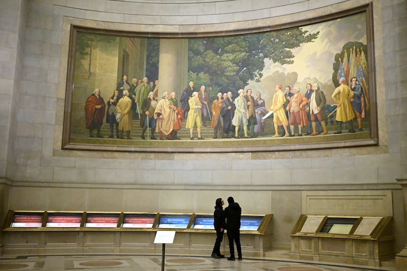 Deux visiteurs regardent les expositions sous une grande fresque murale montrant la signature de la Déclaration d'indépendance aux Archives nationales le jeudi 29 janvier 2026, à Washington, D.C.