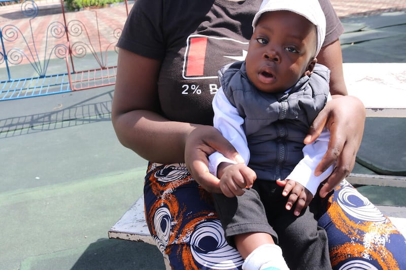 Samuel, âgé d'un an, assis sur les genoux de sa mère devant l'hôpital général Lewanika à Mongu, en Zambie. Il est né prématurément en décembre 2024.