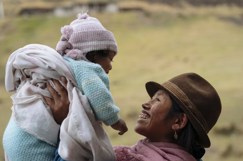 Une femme en vêtements traditionnels tient son enfant en Équateur.
