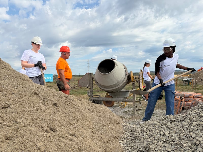Des jeunes adultes préparent du béton sous la direction d'un professionnel du bâtiment de Habitat for Humanity Roumanie lors d'un projet de service d'une semaine à Berceni, en Roumanie, en août 2026.