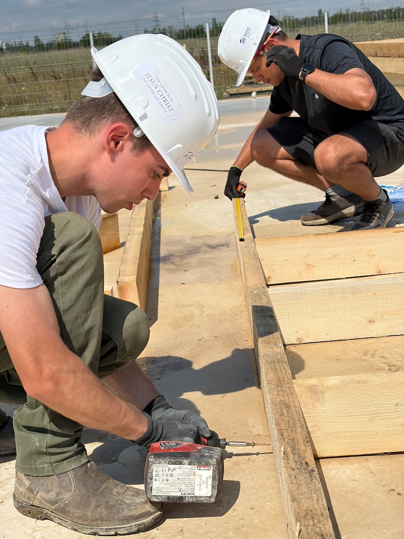 Des jeunes adultes mesurent et assemblent des ossatures de murs en bois pour des maisons en construction dans le cadre d'un projet de service d'Habitat pour l'humanité Roumanie à Berceni, en Roumanie, en août 2026.