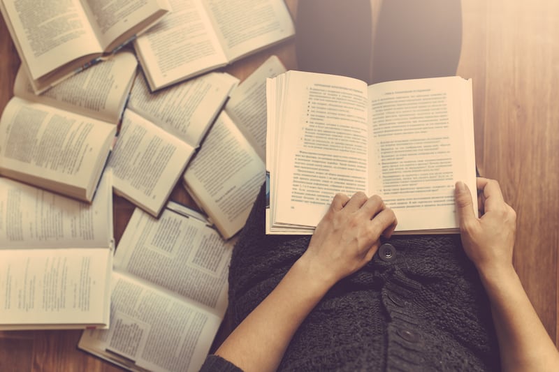 Une femme lit un livre avec plusieurs livres sur le sol autour d'elle.
