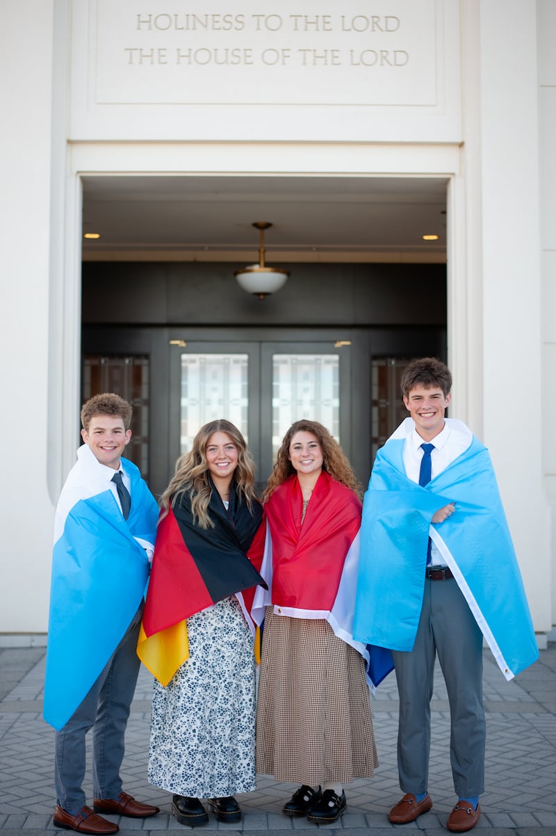 Isaac, Elle, Isabel et Eli Reid posent pour une photo avec des drapeaux représentant les lieux où ils serviront en mission drapés autour de leurs épaules.