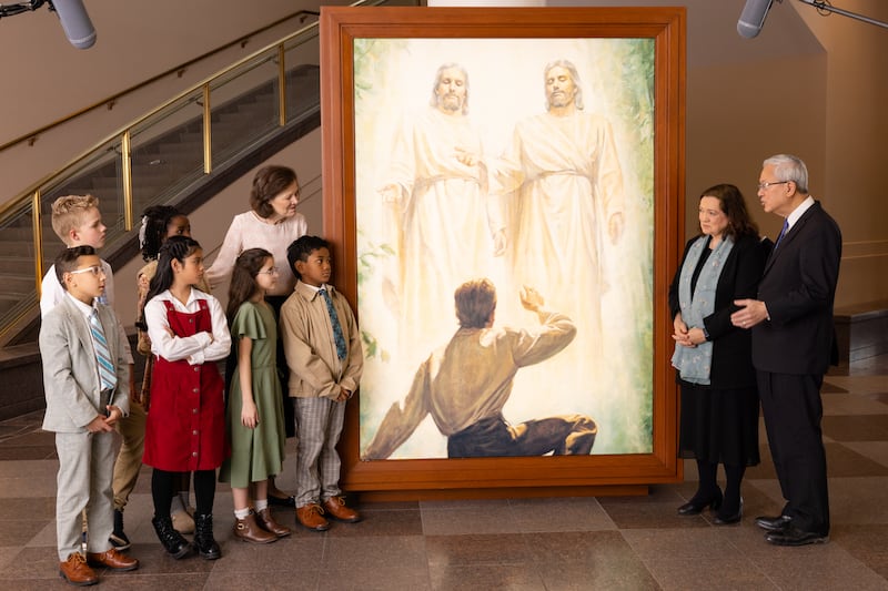 Elder Gerrit W. Gong, Sister Susan Gong, and President Susan H. Porter talk with six children by a portrait of the First Vision in the Conference Center in Salt Lake City during the filming of the Friend to Friend, released Sunday, May 24, 2026.