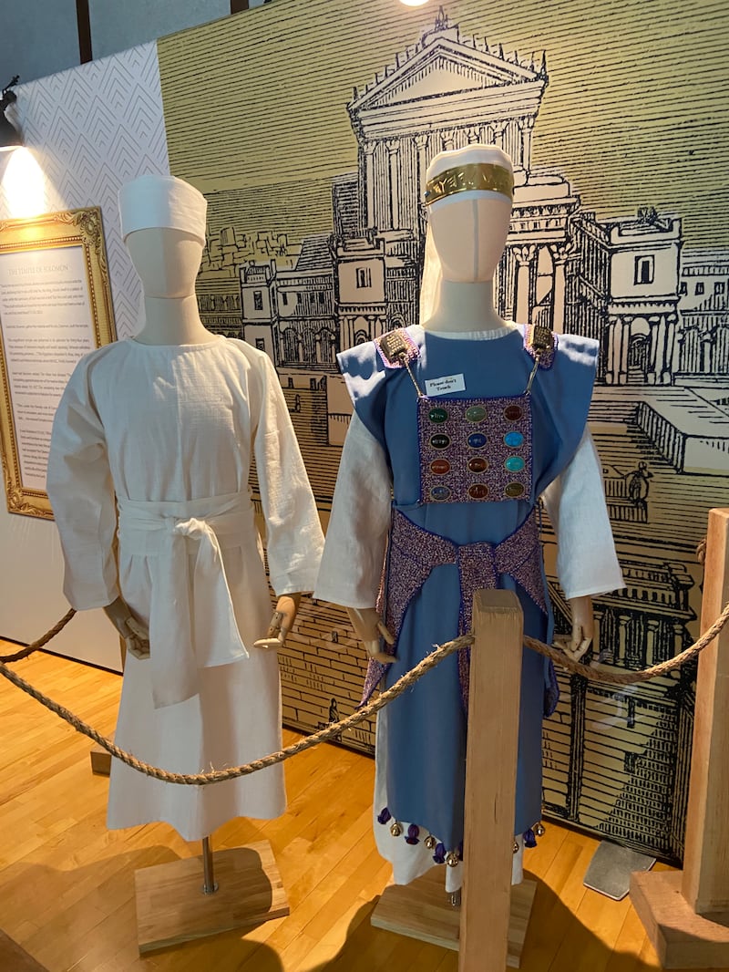 Un mannequin portant une robe blanche et un mannequin portant une robe bleue avec 12 pierres colorées sur le devant, dans la maquette de l'ancien tabernacle itinérant de Moïse.