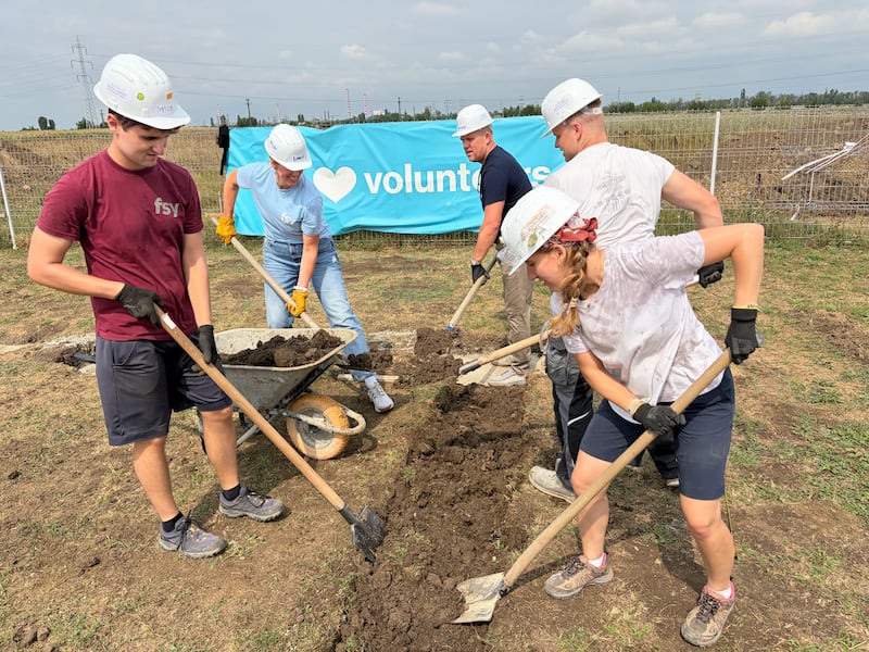 Latter-day Saint volunteers work alongside a Habitat for Humanity Romania construction professional to prepare wooden wall frames for homes under construction in Berceni, Romania, in August 2026.