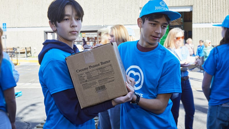 Deux jeunes hommes déplacent des cartons d'un don alimentaire America250 dans la région d'Irvine, en Californie, le samedi 21 février 2026.