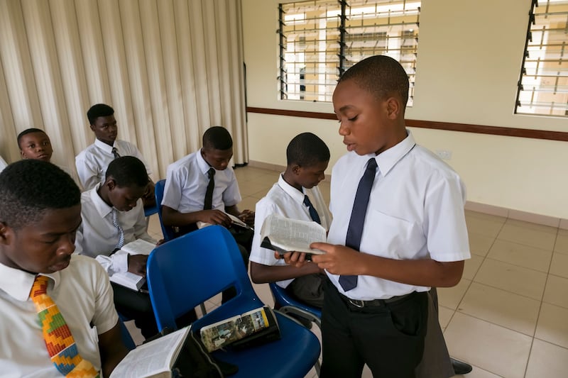 Un groupe de jeunes gens est assis dans un cours de la pretrise au Ghana. Un jeune homme est debout et lit les Ecritures.