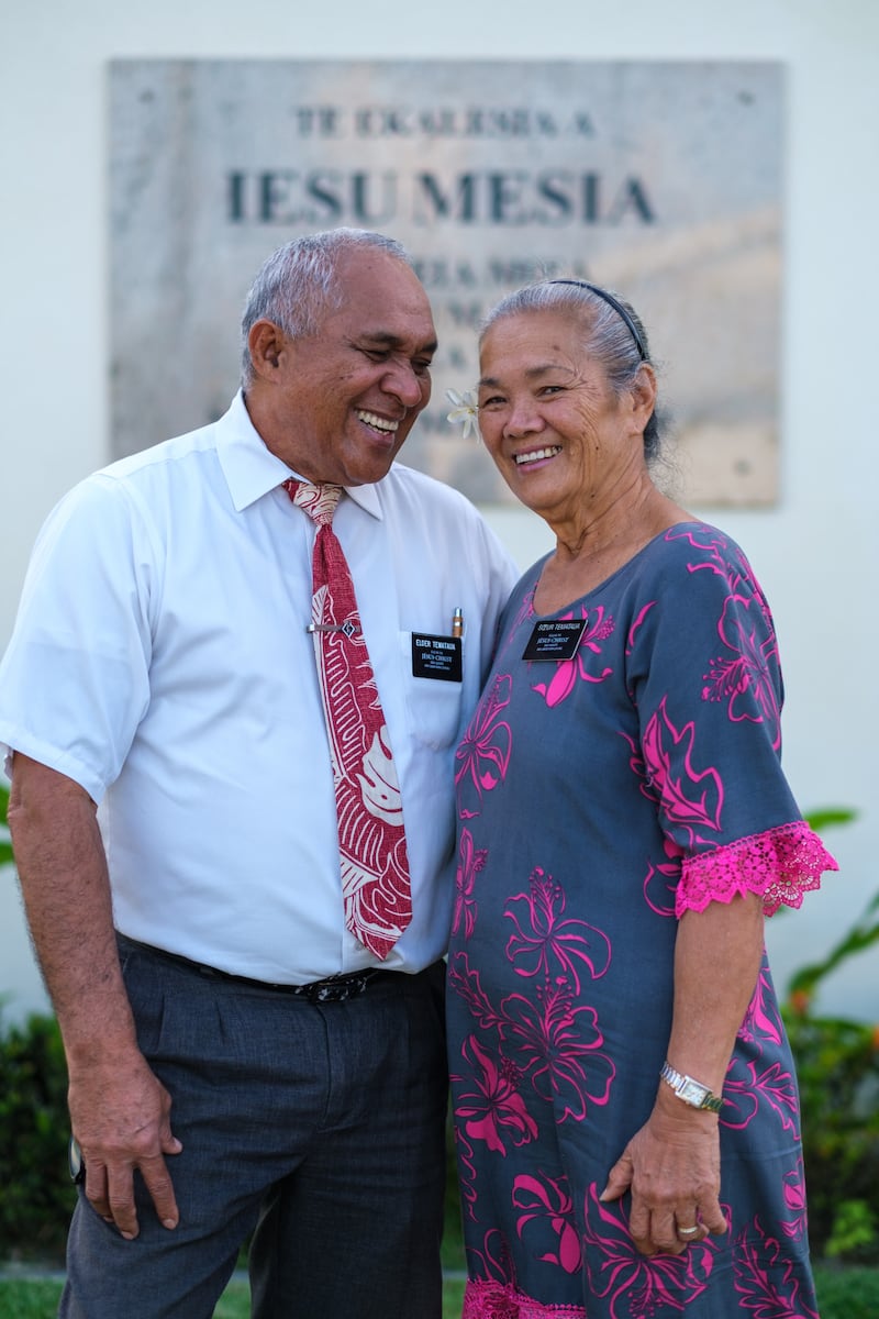 Un couple de missionnaires d’âge mûr se tient près d’une église des saints des derniers jours à Tahiti en 2026.