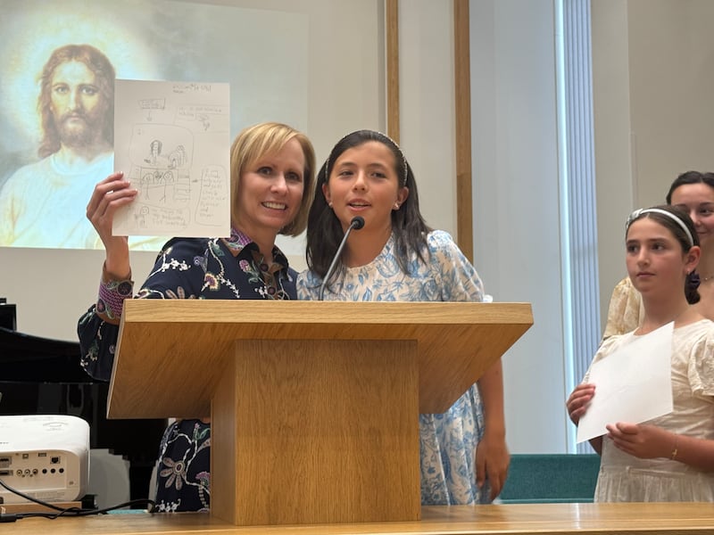 Sœur Amy A. Wright, première conseillère dans la présidence générale de la Primaire, se tient au pupitre avec un enfant de la Primaire pendant une réunion spirituelle pour les enfants de la Primaire à Breda (Pays-Bas), le 6 septembre 2025.
