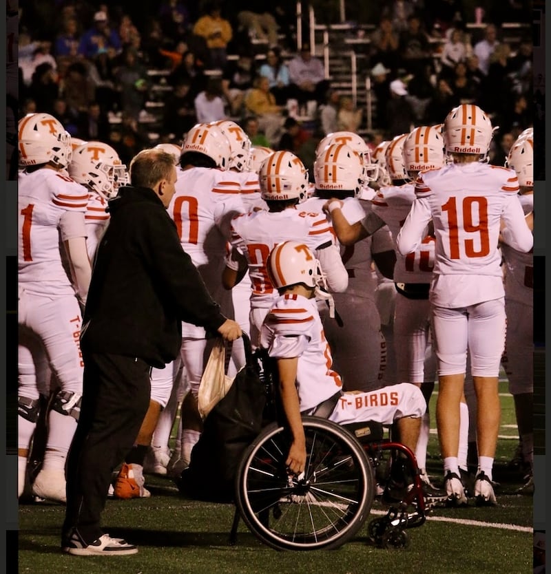 Ken Cooper pousse son fils, Matthew Cooper, dans son fauteuil roulant sur la ligne de touche lors d'un match de football américain du lycée Timpview à Provo (Utah), à l'automne 2024.
