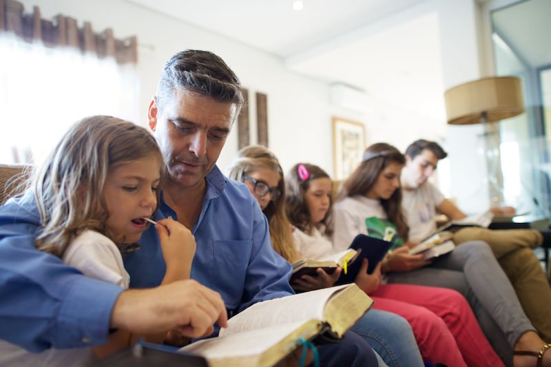 Un père est assis avec ses enfants dans leur salon pour lire les Écritures ensemble au Portugal.