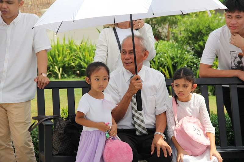 Un grand-père est assis sous un parapluie avec deux filles sur le terrain du temple de Davao, aux Philippines, le dernier jour des portes ouvertes, le 10 avril 2026.