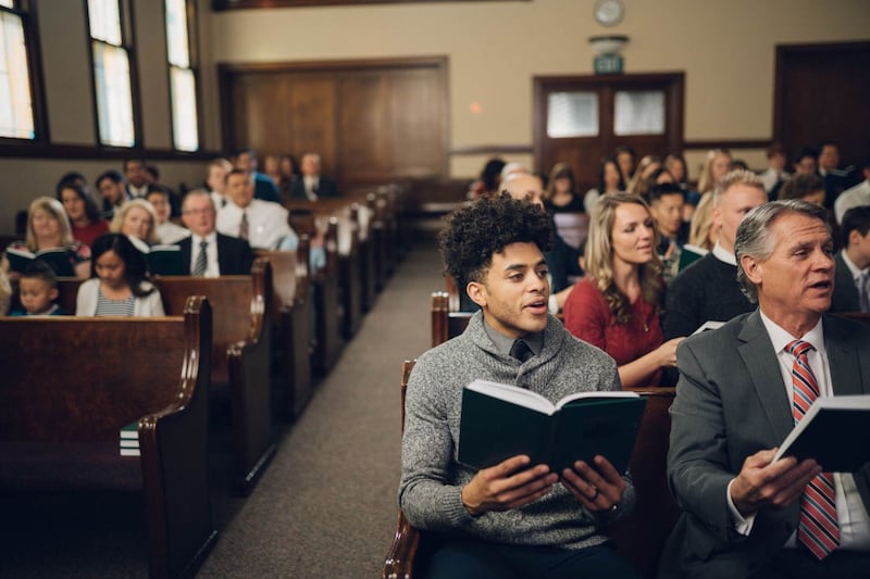 Des personnes sont assises sur les bancs d’une église et chantent en assemblée.
